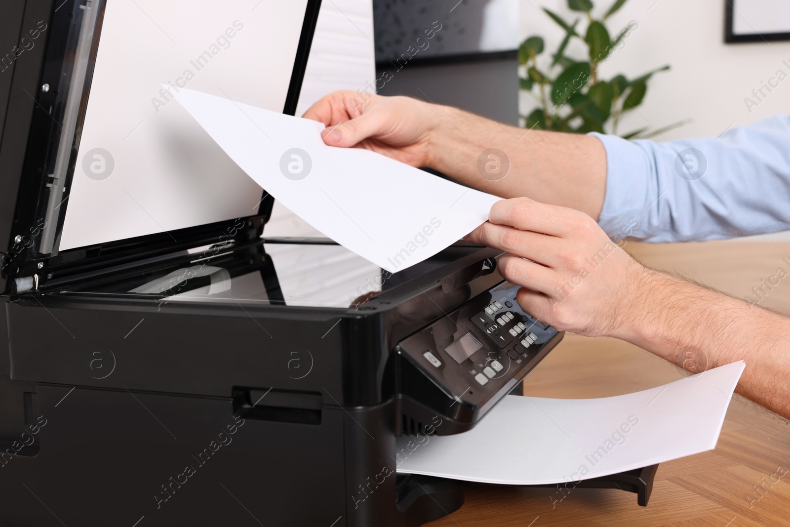 Photo of Man using modern printer at wooden table indoors, closeup