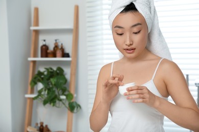 Photo of Beautiful young Asian woman holding body cream in room, space for text