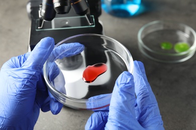 Photo of Medical assistant holding laboratory glassware with sample at table, closeup