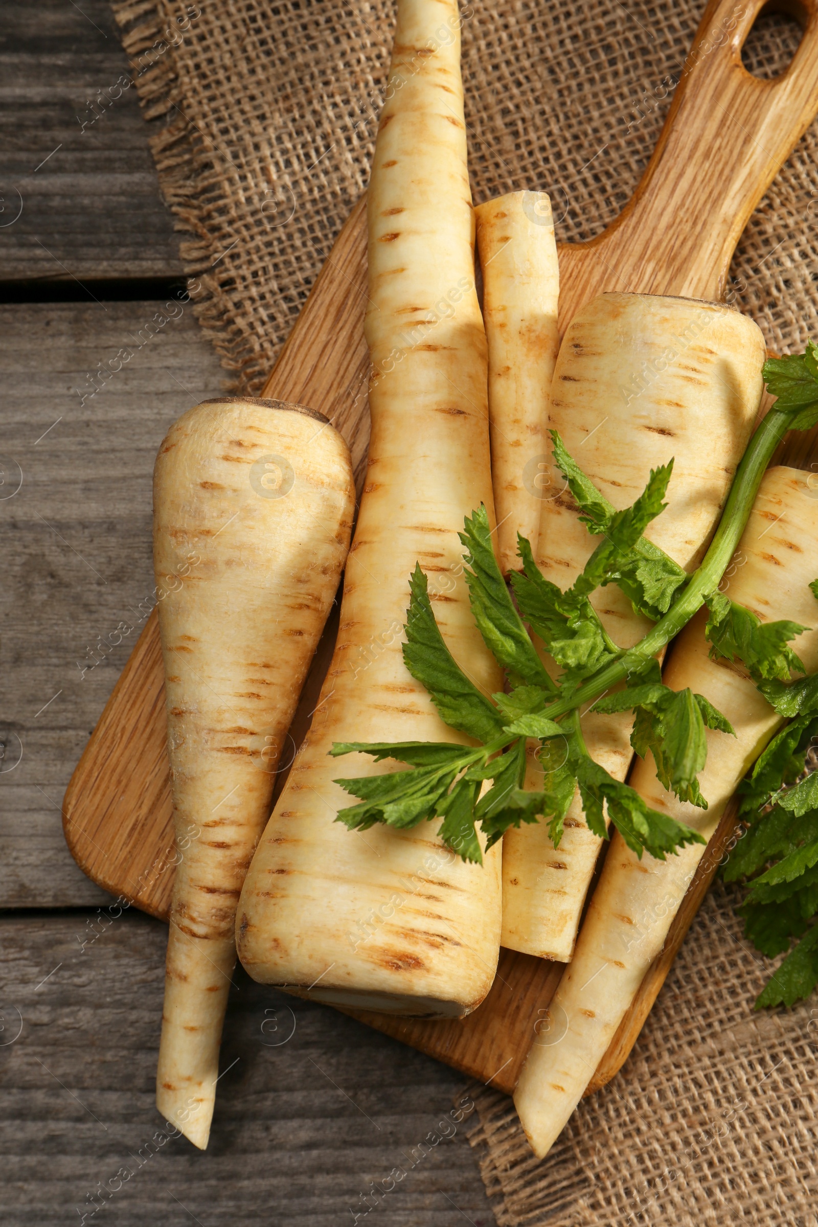 Photo of Many fresh ripe parsnips and green leaves on wooden table, flat lay