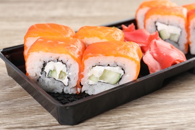 Box with tasty sushi rolls on wooden table. Food delivery