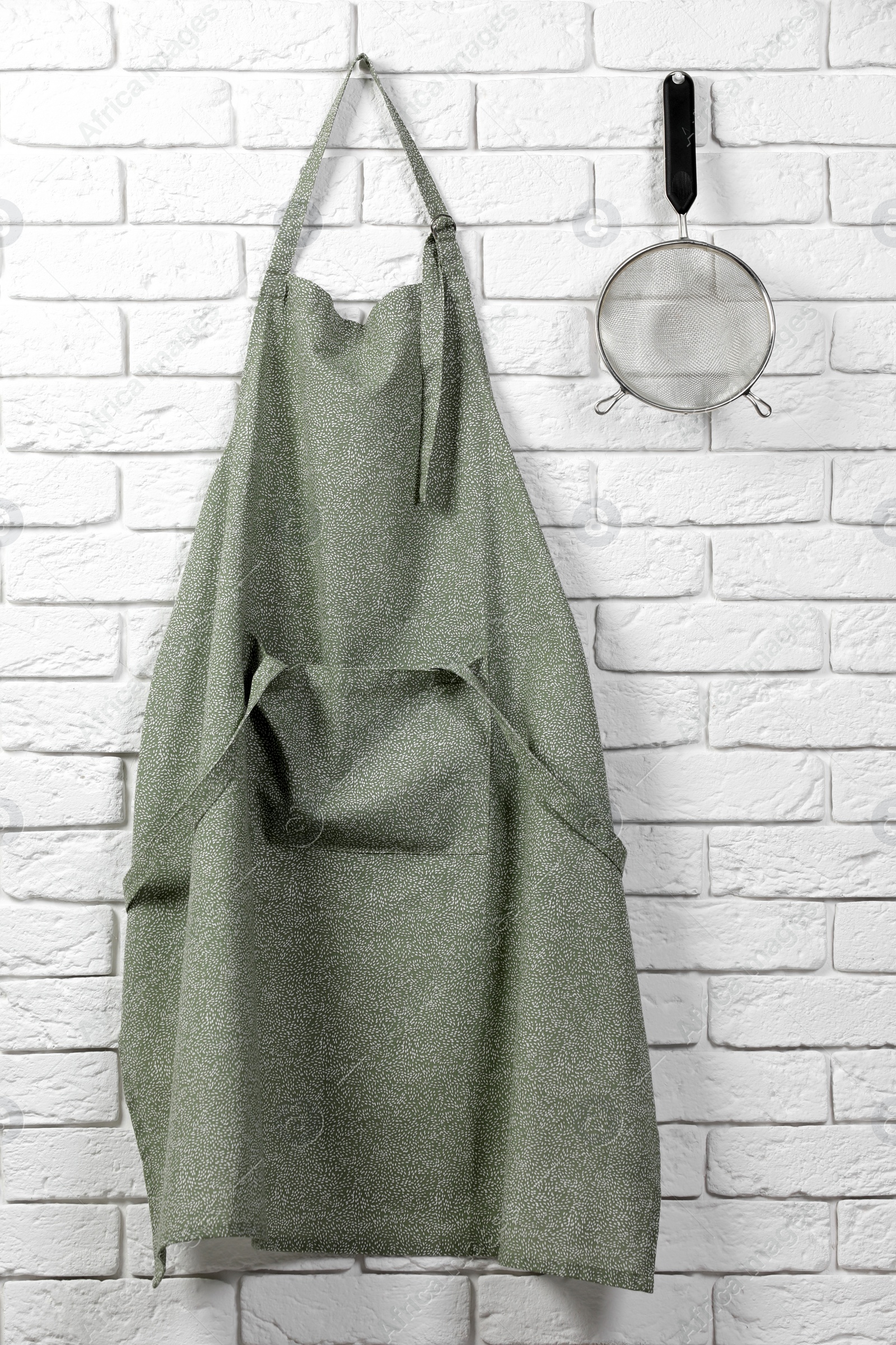 Photo of Clean kitchen apron with pattern and sieve on white brick wall