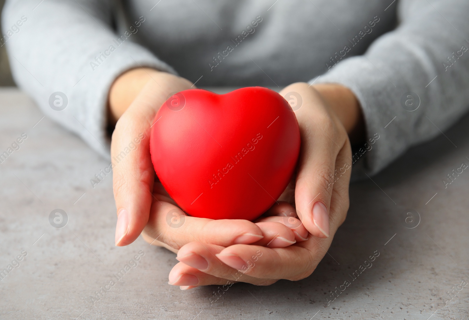 Photo of Woman holding red heart on gray table, closeup. Cardiology concept