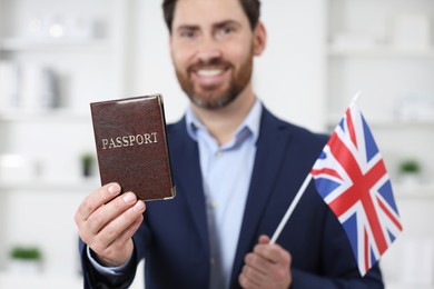 Photo of Immigration. Happy man with passport and flag of United Kingdom indoors, selective focus