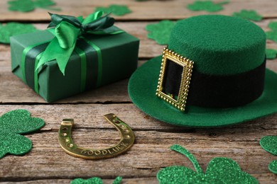 Photo of St. Patrick's day. Leprechaun hat, golden horseshoe, green gift box and decorative clover leaves on wooden background