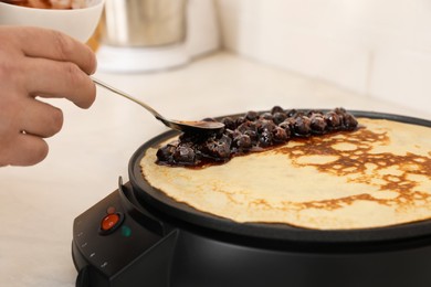 Photo of Man cooking delicious crepe with jam on electric pancake maker in kitchen, closeup