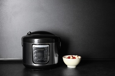 Modern multi cooker and ingredients on table near dark wall, space for text