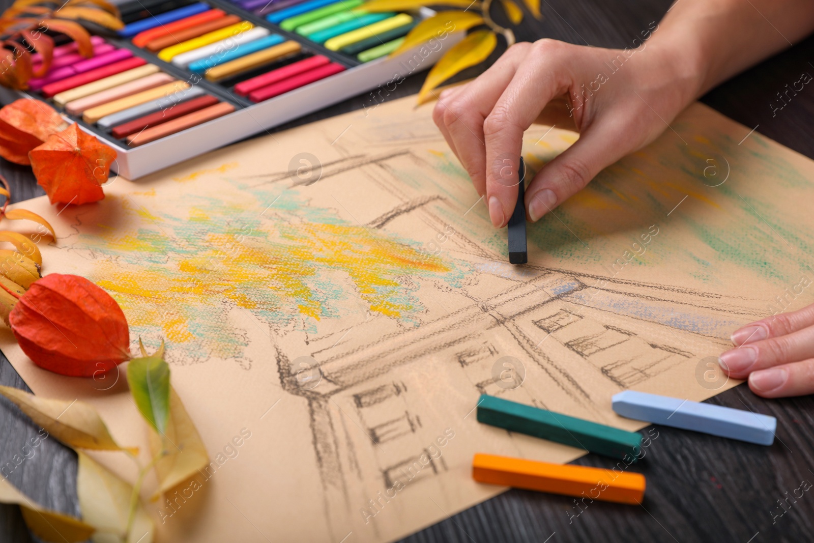Photo of Woman drawing beautiful building with soft pastel at wooden table, closeup