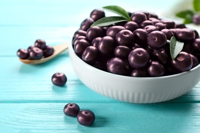 Tasty acai berries in bowl on light blue wooden table, closeup