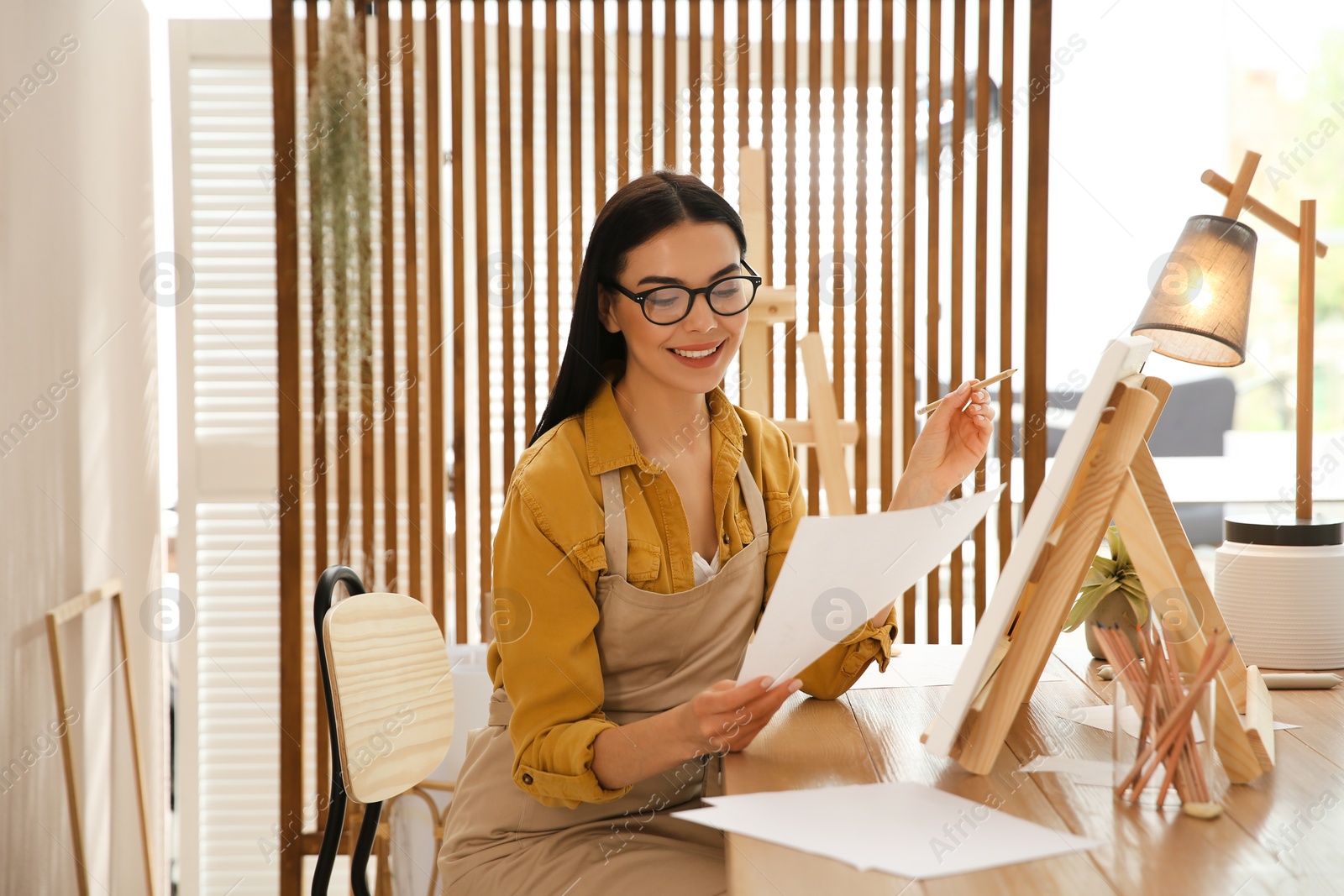 Photo of Young woman drawing on easel with pencil at table indoors