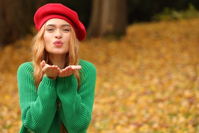 Photo of Portrait of beautiful woman blowing kiss in autumn park. Space for text
