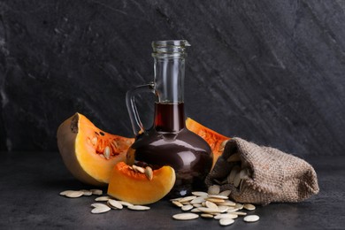 Photo of Fresh pumpkin seed oil in glass jug on dark grey table