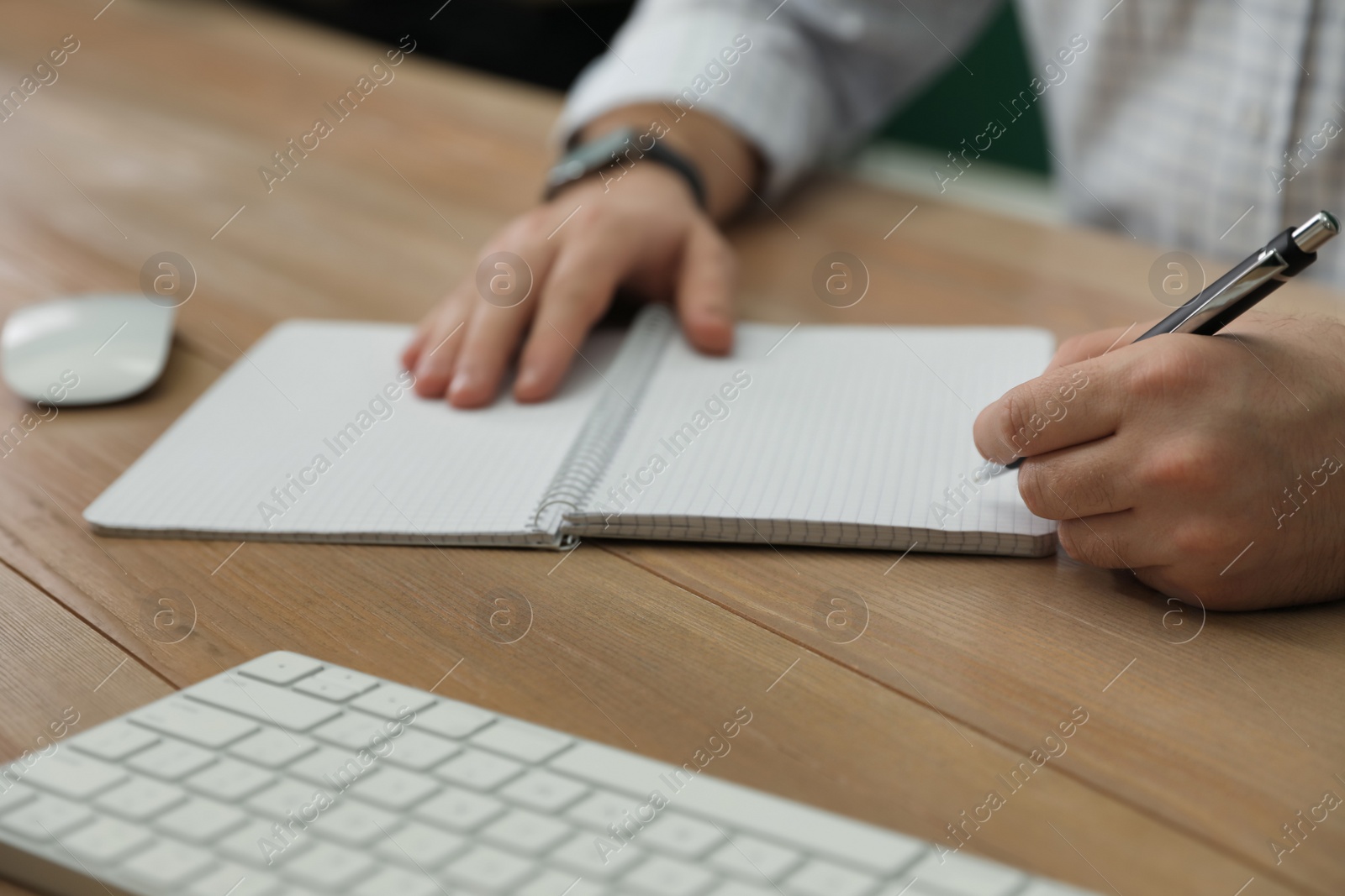 Photo of Left-handed man writing in notebook at wooden table, closeup