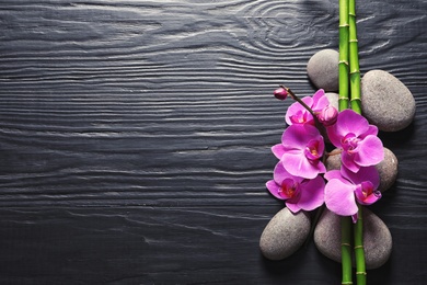 Photo of Spa stones with orchid flowers and bamboo on dark wooden background, top view. Space for text