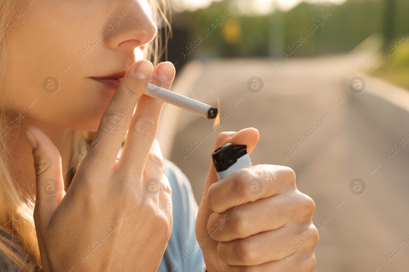 Photo of Young woman lighting cigarette outdoors, closeup of hands