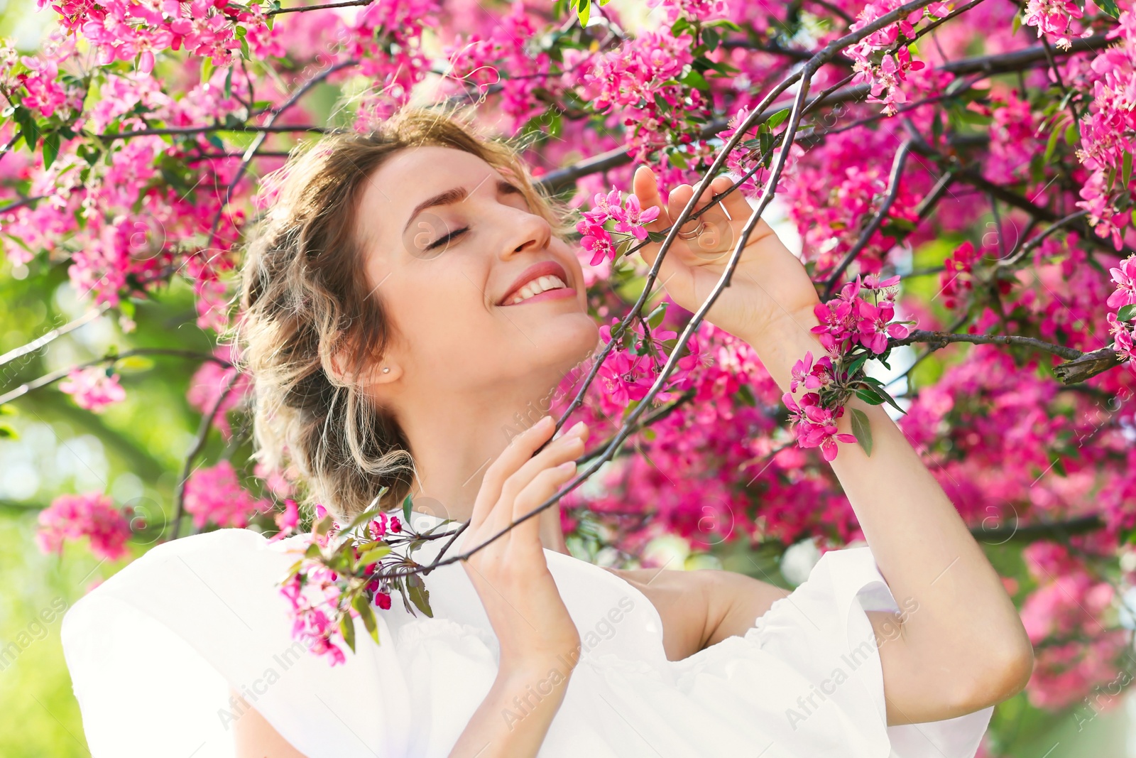 Photo of Attractive young woman posing near blossoming tree on sunny spring day