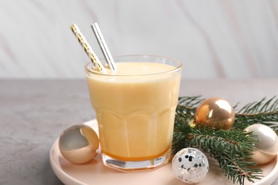 Glass of delicious eggnog and decorated fir branch on gray table