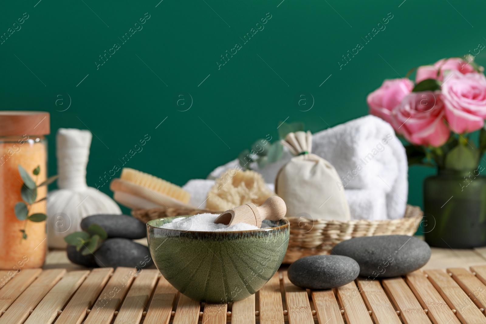 Photo of Beautiful composition with sea salt, flowers and different spa products on wooden table near green wall, space for text