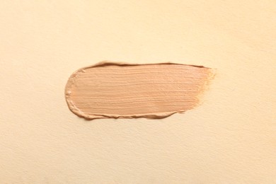 Photo of Smear of skin foundation on beige background, top view