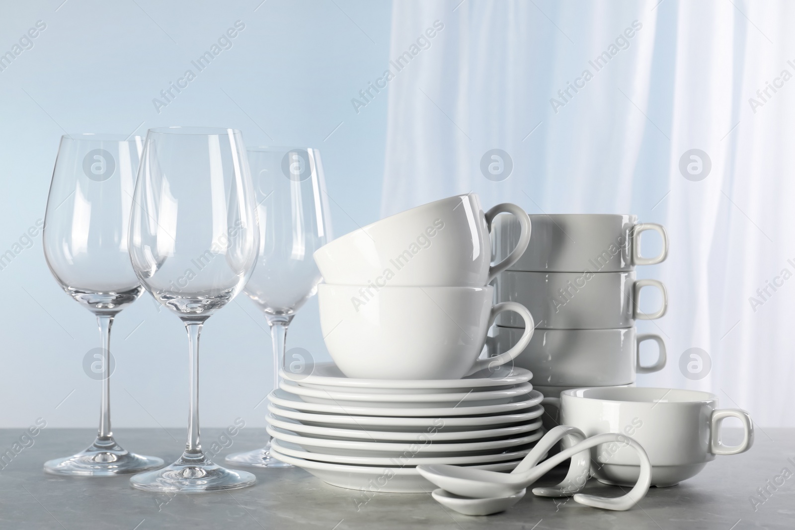 Photo of Set of clean dishware and glasses on grey marble table