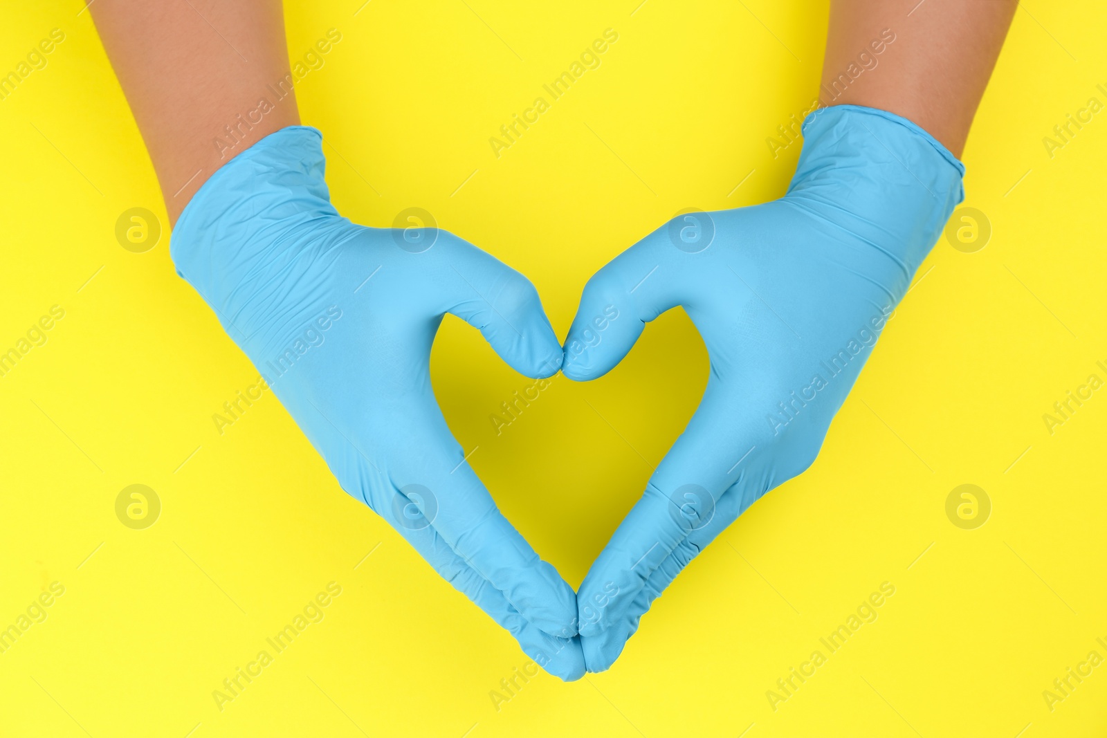 Photo of Person in blue latex gloves showing heart gesture against yellow background, closeup on hands