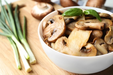 Photo of Delicious cooked mushrooms with basil in bowl on table, closeup. Space for text