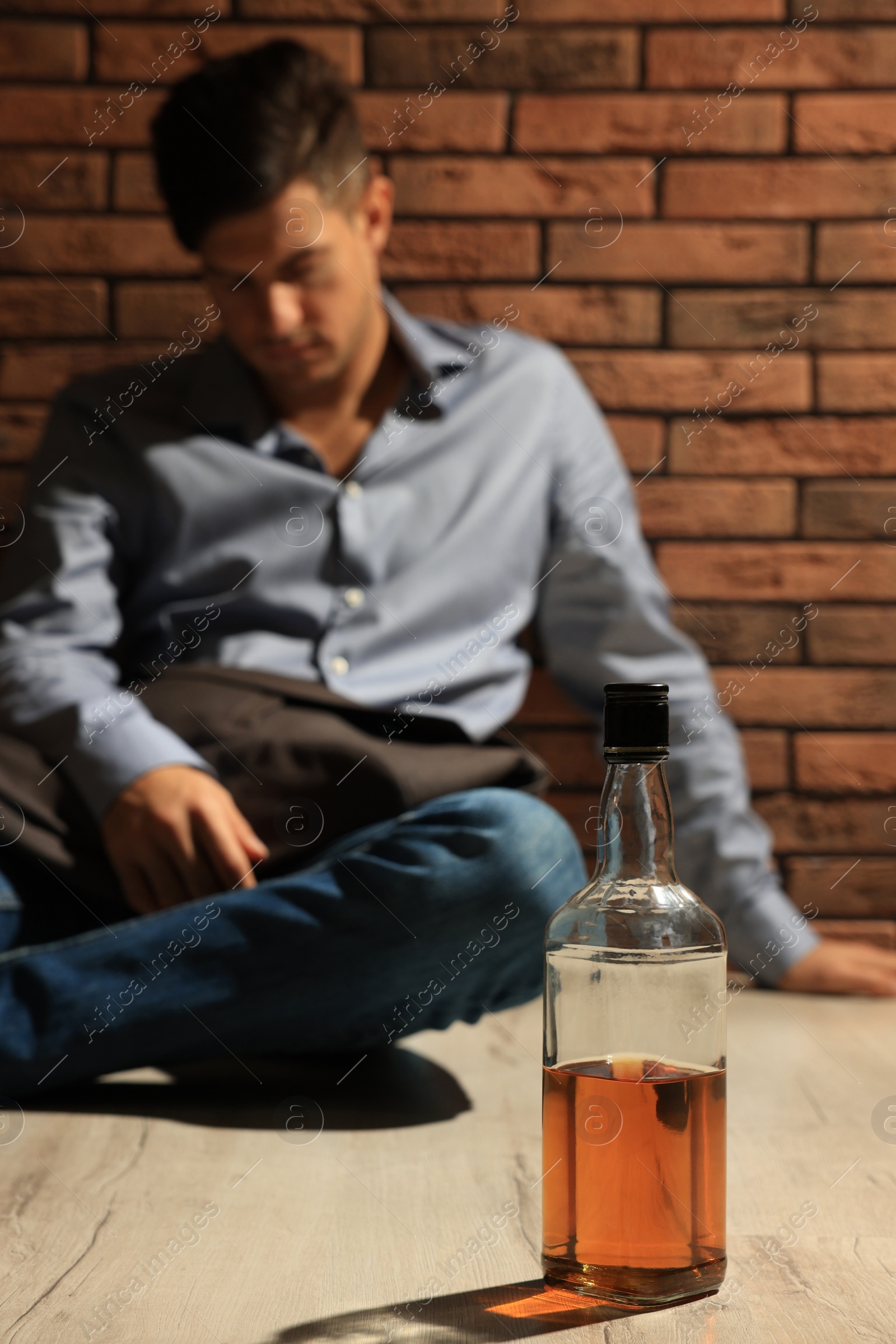 Photo of Addicted man sitting near red brick wall, focus on bottle of alcoholic drink