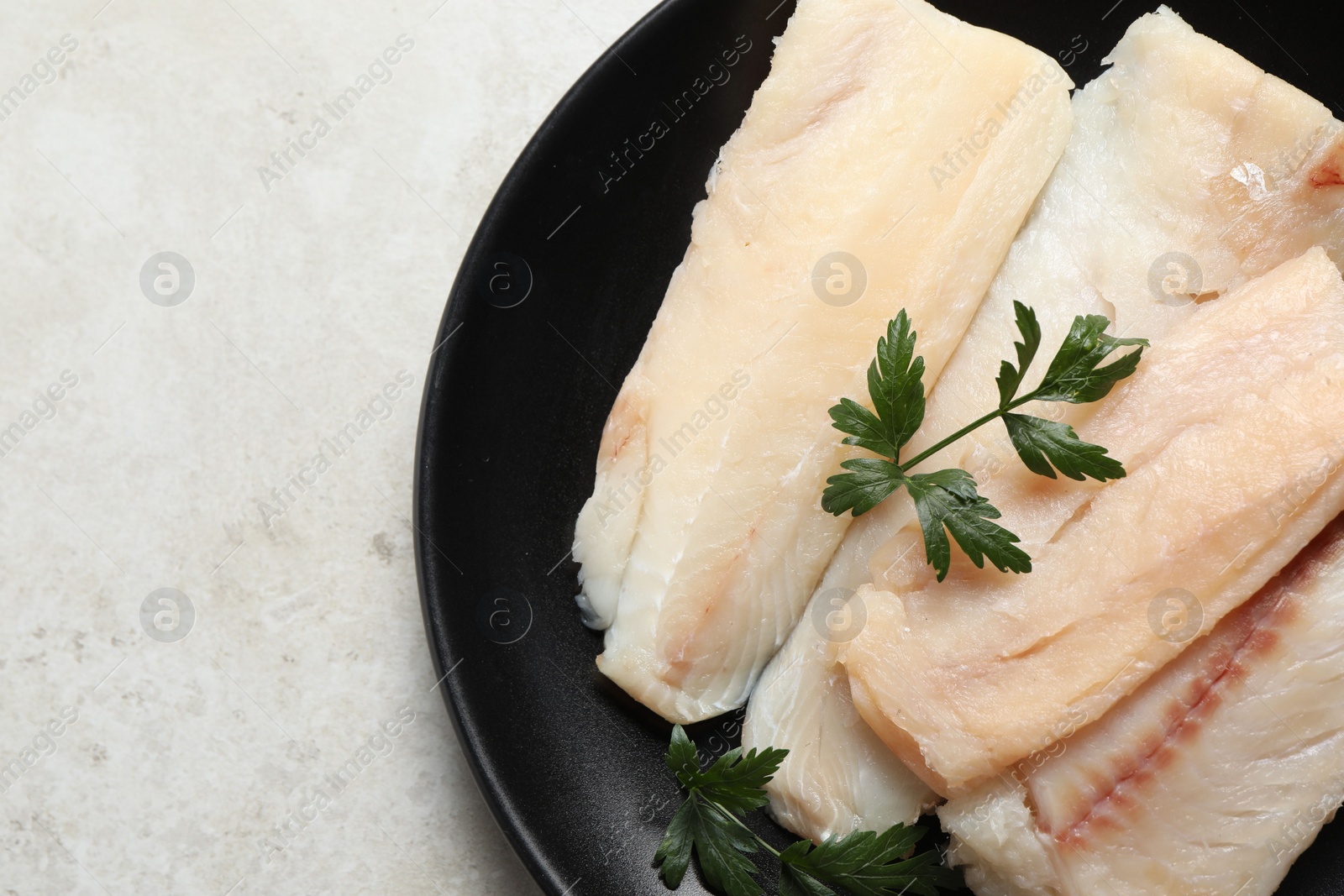 Photo of Plate with raw cod fish and parsley on light textured table, top view. Space for text