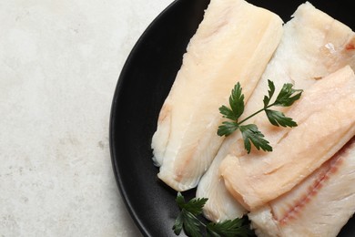 Plate with raw cod fish and parsley on light textured table, top view. Space for text