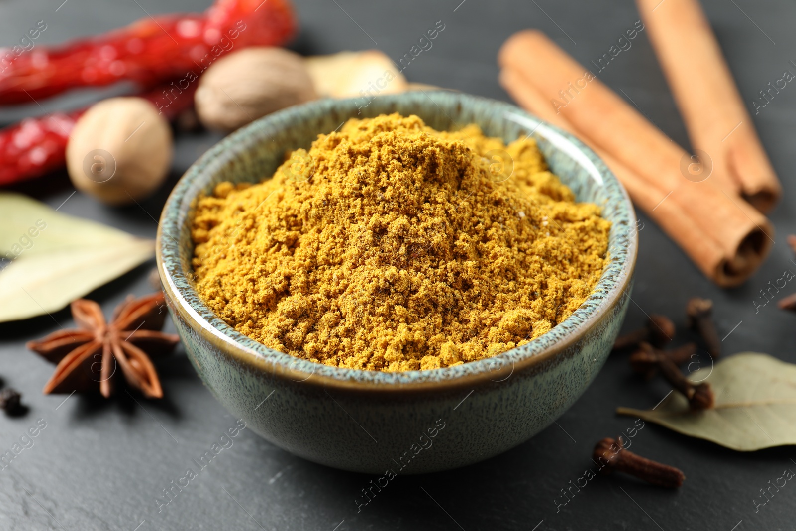 Photo of Dry curry powder in bowl and other spices on dark table, closeup
