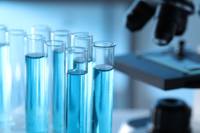 Photo of Test tubes with light blue liquid near microscope in laboratory, closeup