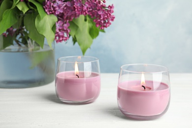 Burning wax candles in glass holders and flowers on white table