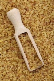 Wooden scoop with cereal on uncooked bulgur, top view