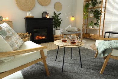 Photo of Stylish fireplace near comfortable armchairs and coffee table with tea in cosy living room. Interior design