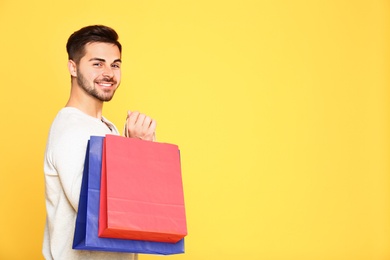 Photo of Portrait of young man with paper bags on yellow background. Space for text
