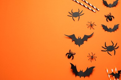 Photo of Flat lay composition with paper bats, spiders and straws on orange background, space for text. Halloween celebration
