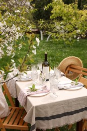 Photo of Stylish table setting with beautiful spring flowers, wine, plates and glasses in garden