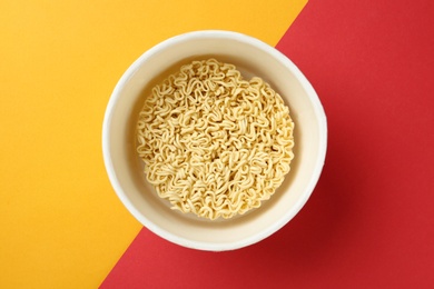 Cup of instant noodles on color background, top view