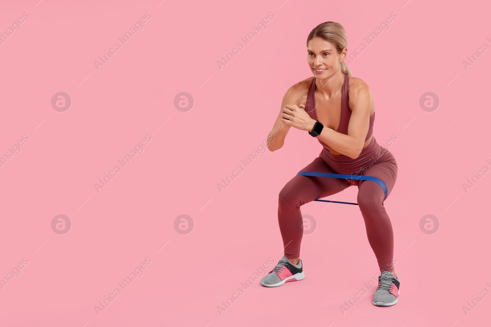 Photo of Woman exercising with elastic resistance band on pink background. Space for text