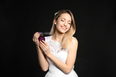 Photo of Beautiful young bride applying perfume against black background