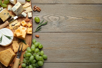 Cheese platter with specialized knife and fork on wooden table, flat lay. Space for text