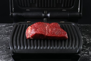Photo of Cooking fresh beef cut on electric grill at black table