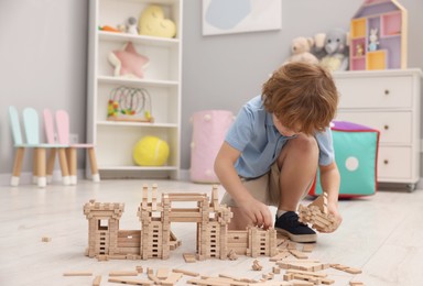 Little boy playing with wooden construction set on floor in room, space for text. Child's toy
