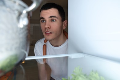 Man near refrigerator in kitchen at night, view from inside