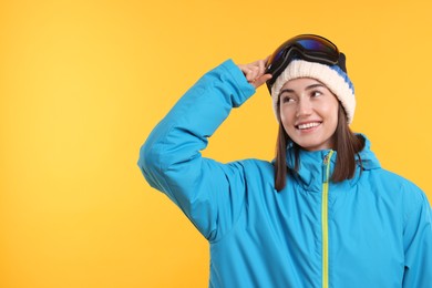 Photo of Winter sports. Happy woman with snowboard goggles on orange background, space for text