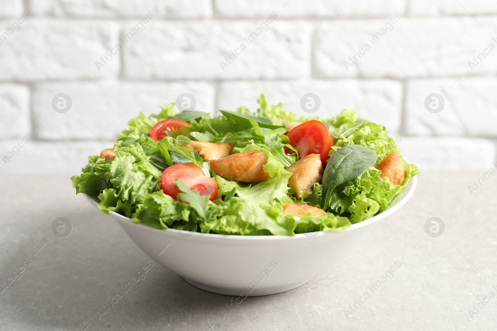 Photo of Delicious salad with chicken and cherry tomato on light grey table, closeup