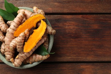 Photo of Bowl with fresh turmeric roots and leaves on wooden table, top view. Space for text