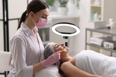 Photo of Cosmetologist applying mask on woman's face in clinic