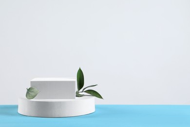 Photo of Podium with green leaves on light blue wooden table. Space for text