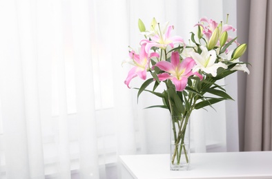 Photo of Vase with bouquet of beautiful lilies on white table indoors. Space for text